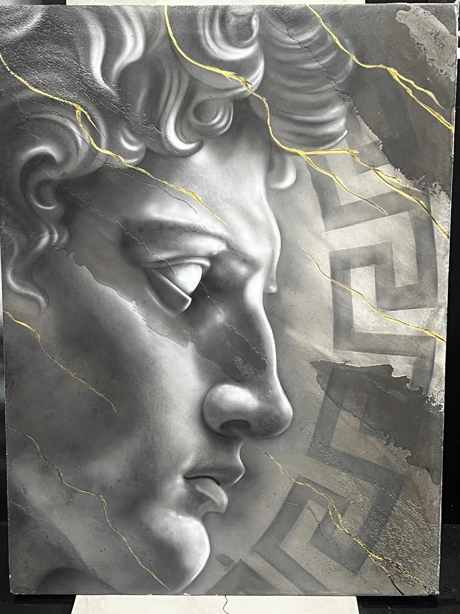 Sculpted classical face in plaster with gold veining over a Greek key border