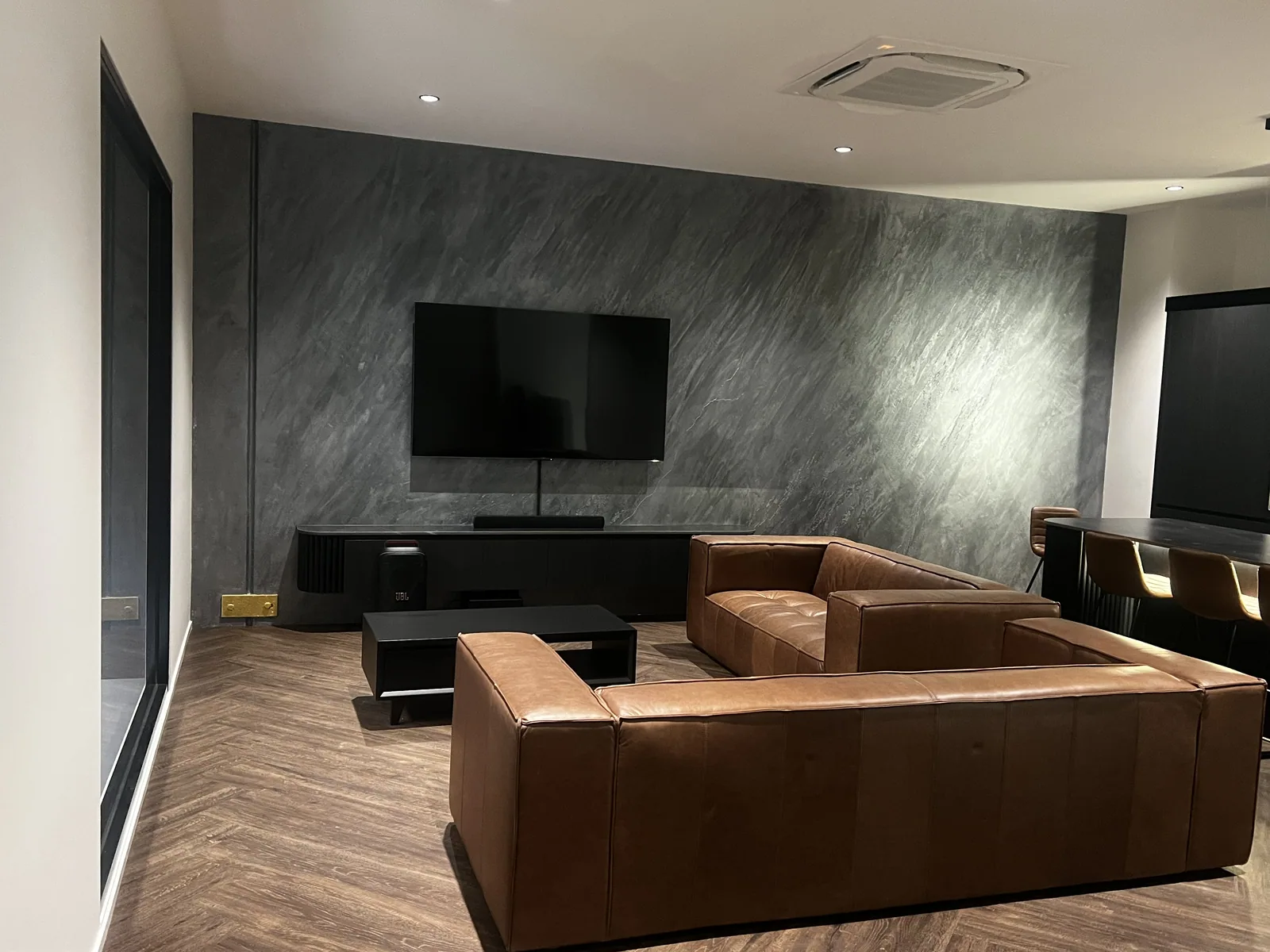 Charcoal textured feature wall behind a leather lounge and television