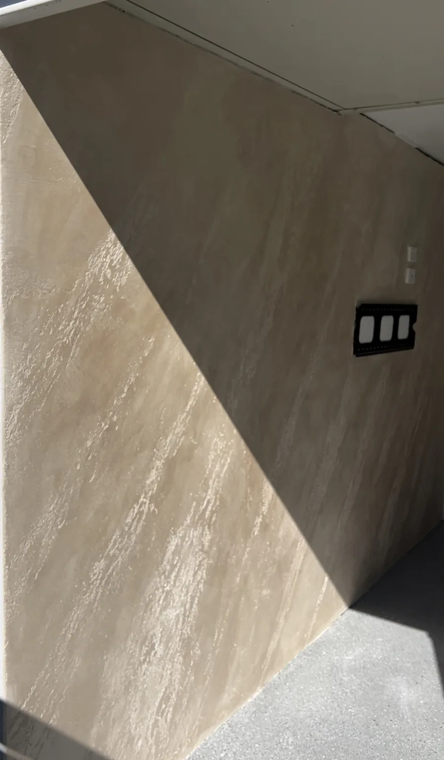 Sand-toned travertine-look Venetian plaster wall in raking light