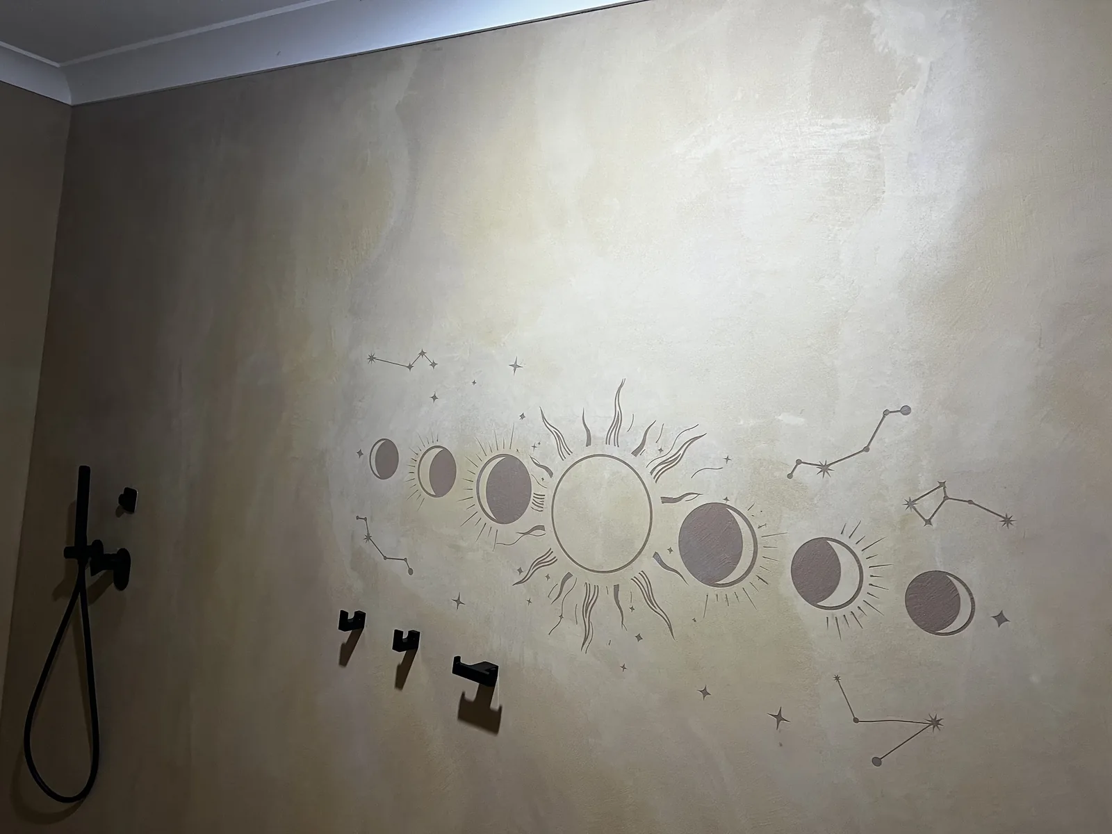 Cream micro cement bathroom wall with an airbrushed sun, moon phase and constellation mural