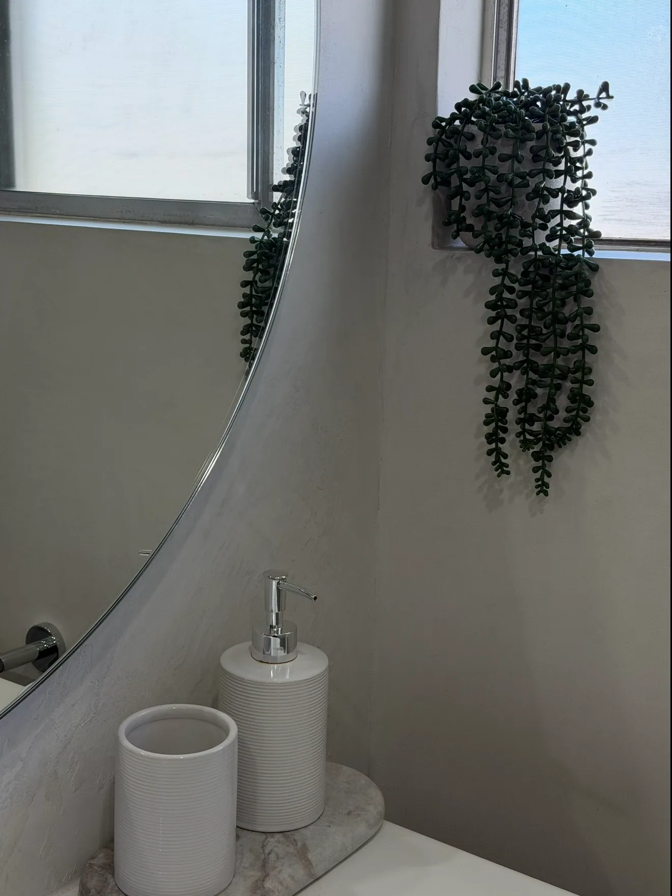 Curved micro cement vanity wall with a trailing plant above