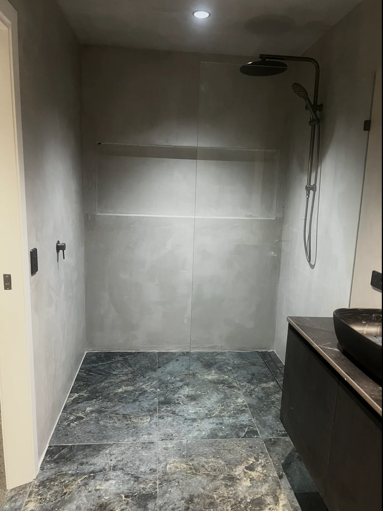 Micro cement shower with black tapware and a marble-look floor