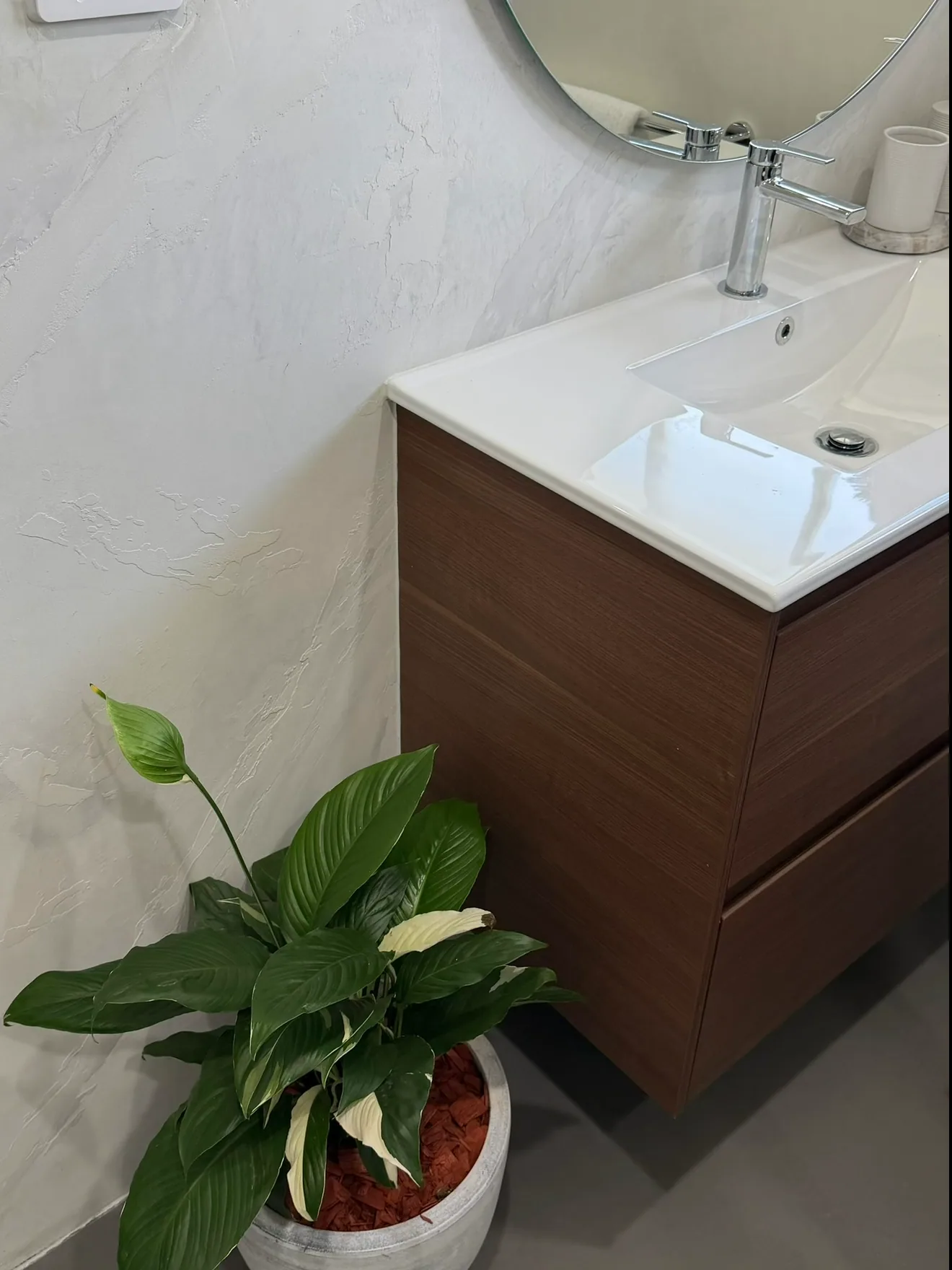 Micro cement bathroom wall behind a timber vanity and round mirror